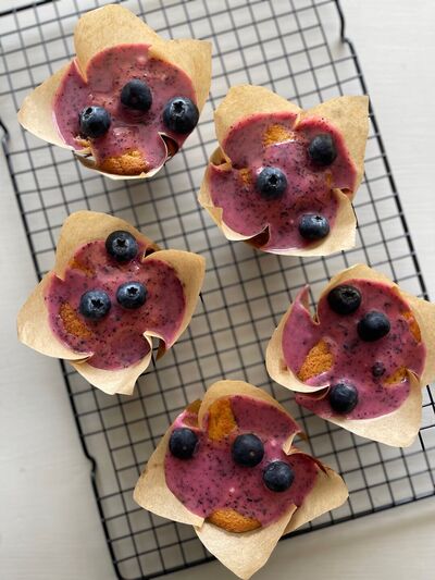 Blueberry cupcakes in paper cases, topped with fresh blueberries, cooling on a wire rack
