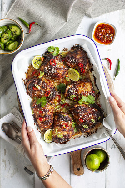 Sticky glazed chicken thighs with sliced chilli, spring onion and lime in a white roasting dish