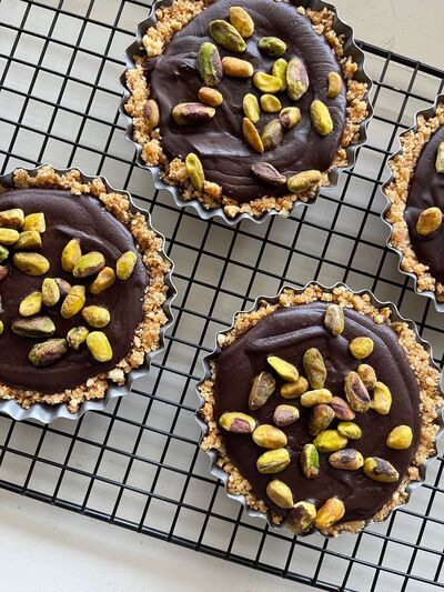 No-bake chocolate tarts in biscuit cases topped with pistachios, on a wire cooling rack