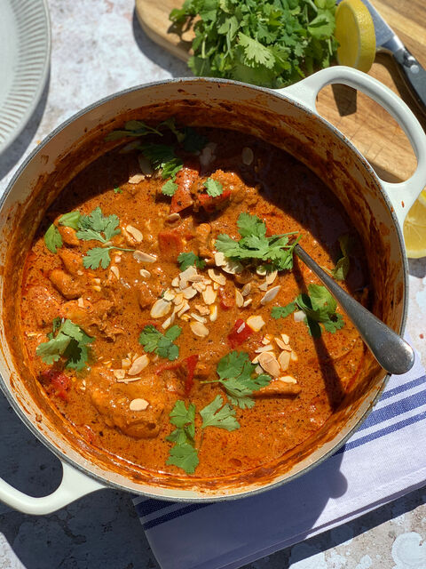 A pot of creamy orange curry topped with flaked almonds and coriander, with a spoon in the pot