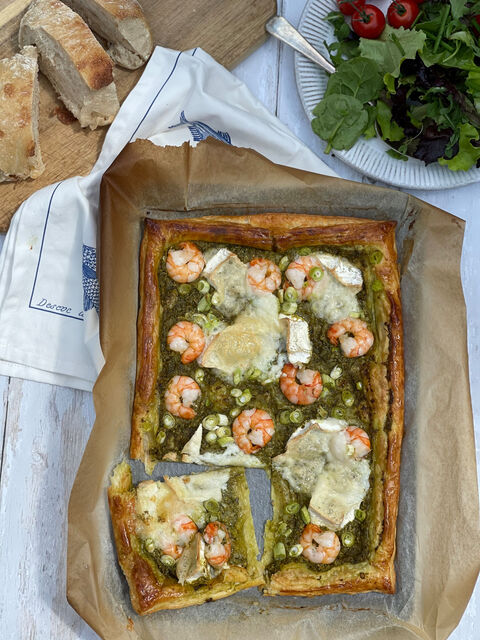 A rectangular puff-pastry tart with green pesto, prawns and melted cheese, with one slice cut