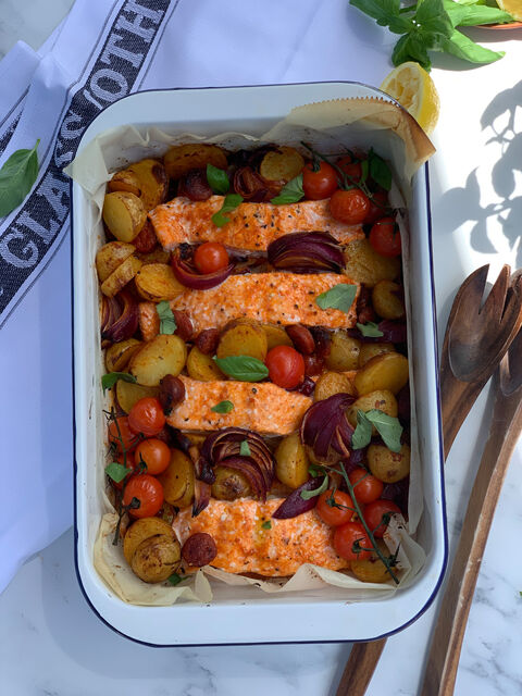 An enamel tray of salmon fillets roasted with baby potatoes, cherry tomatoes and red onion
