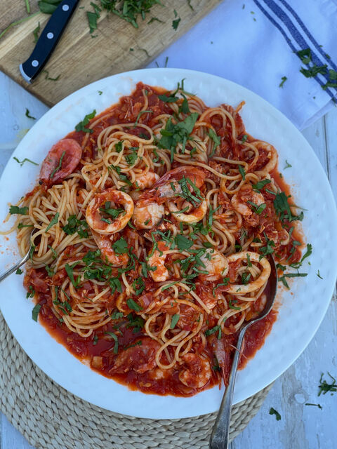 Spaghetti with prawns, squid rings and tomato sauce, sprinkled with chopped herbs, on a white plate