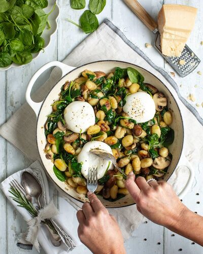 Golden gnocchi with spinach, mushrooms and torn burrata in a white enamel pan