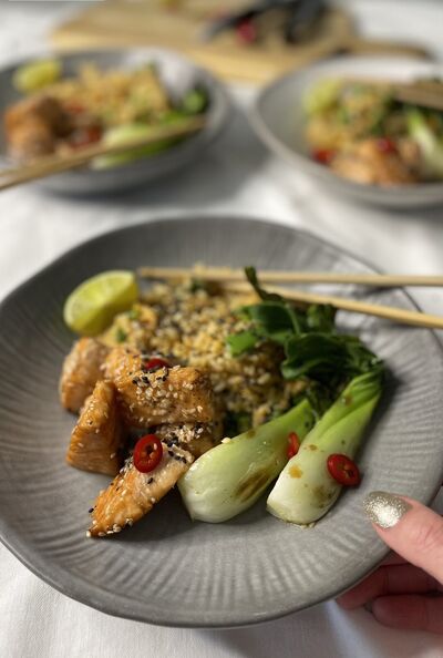 Salmon and egg fried rice in a grey bowl with pak choi, lime and chopsticks