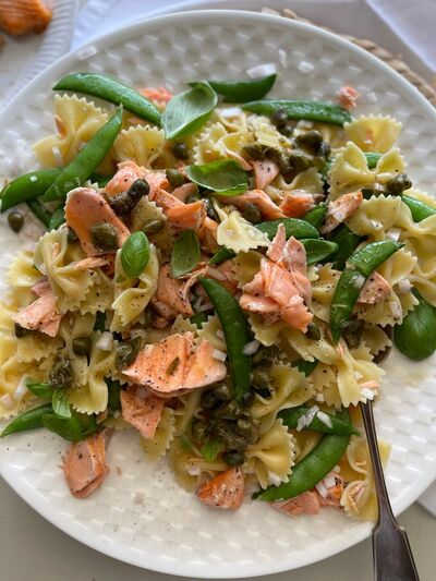 Farfalle pasta salad with flaked salmon, sugar snap peas, capers and basil on a white plate